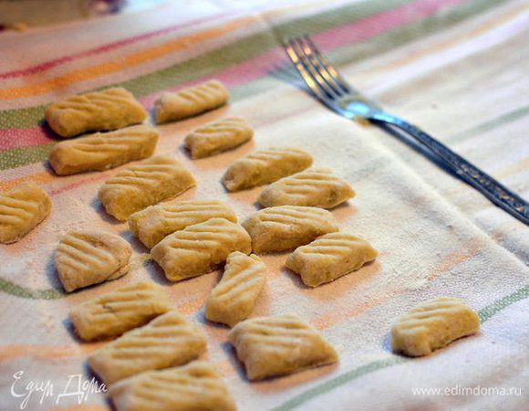 В кастрюлю кладем картофель в кожуре, заливаем холодной водой, отвариваем до готовности (от момента закипания около 30 — 40 минут). Примерно за 10 минут до окончания варки картофеля, начинаем готовить соус (рецепт ниже).
Очищаем от кожуры (я нанизываю его для этого на вилку, чтобы не обжечь руки), разминаем. Добавляем яйцо, муку, соль, вымешиваем тесто. Отделяем немного теста и скатываем его в колбаску, колбаску нарезаем на квадратики около 2 см. В Италии продается специальная деревянная дощечка с полосками, по которой раскатывают ньокки, чтобы сделать на них полосочки. Для этой цели можно использовать обычную вилку: прокатываем готовый комочек теста сверху-вниз. Готово!