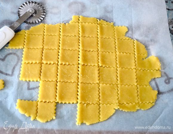 Раскатать оставшееся тесто. Фигурным ножом нарезать раскатанное тесто на квадратики (сначала нарезать на полоски в одном направлении, а затем развернуть тесто и снова нарезать, создав таким образом квадраты с одинаковой стороной). 