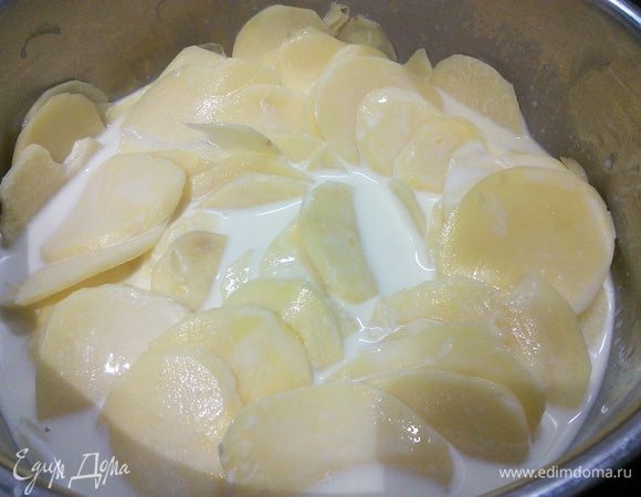 В это время займётся начинкой.  Картофель очистить и тонко порезать кружочком. Удобно воспользоваться блендером с прилагающийся для этого насадкой.  Кастрюлю со сливками поставить на огонь. Как только сливки закипят, снять с огня и выложить в них картофель. Накрыть крышкой и оставить в кастрюле с горячими сливками на 15 — 25 минут. Сыр натереть на крупной тёрке.