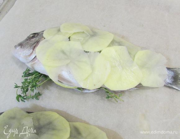 Рыбу выложить на противень, застеленный пекарской бумагой. Поверх каждой рыбы выложить картофель в один слой.