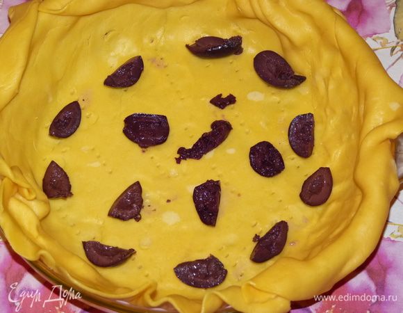 Тесто аккуратно раскатать (лучше на пергаменте или силиконовом коврике) так, чтобы были запасы на края, которые подвернём вовнутрь. Переложить в форму и наколоть вилкой. Оливки нарезать на дольки, выложить на тесто.