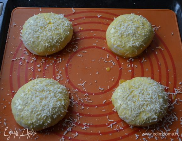 Выложить их на противень, застеленный пекарской бумагой, (или на силиконовый коврик). Смазать булочки яйцом и обильно посыпать натертым на мелкой терке пармезаном.