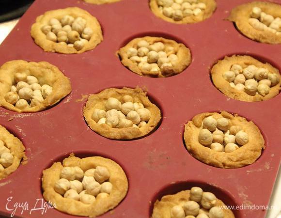 Для того, чтоб тарты при выпечке сохранили форму, лучше внутрь засыпать крупу. Чем мельче, тем лучше. И лучше простелить мятую пекарскую бумагу, а то может пристать и придется отколупывать. Я взяла нут, и тарты внутри были в ямочки от него. Лучше брать тот же рис или пшено.
В духовку на 180°С до готовности. У меня ушло все 30 минут, плюс последние 10 я допекала уже без нута внутри.