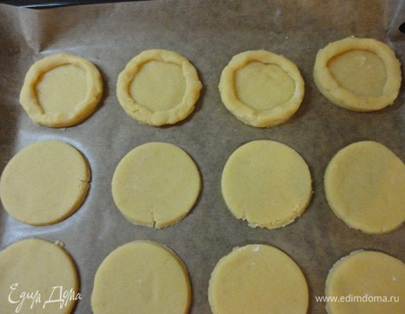 Включить духовку для разогрева до 200°С. Охлажденное тесто раскатать в пласт толщиной 5 мм и тонким стаканом вырезать 18 кружочков. Уложить их на противень, выстланный пекарской бумагой. Края кружочков смазать яичным белком, а из оставшегося теста сформовать тонкие колбаски и выложить в виде бордюрчиков по краям кружочков.