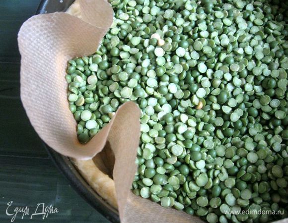 Вырезать из бумаги для выпечки круг по диаметру больше донышка формы, он должен прикрыть и борта формы (лучше это сделать заранее). Положить бумагу на тесто. Насыпать горох (фасоль, рис, потом наполнитель для еды не используется, а хранится для следующей выпечки).
