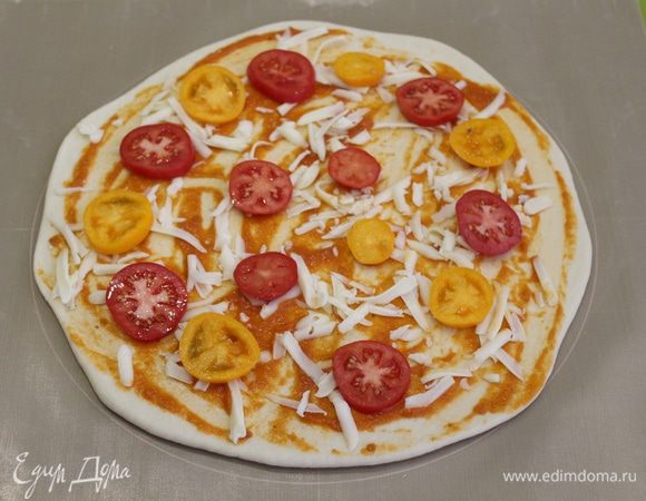 Выложите тесто на подпыленную мукой поверхность и раскатайте до толщины 2 — 3 мм, диаметром около 30 см. Затем тесто намазать томатным соусом, натереть сыр моцарелла, выложить дольки помидор.