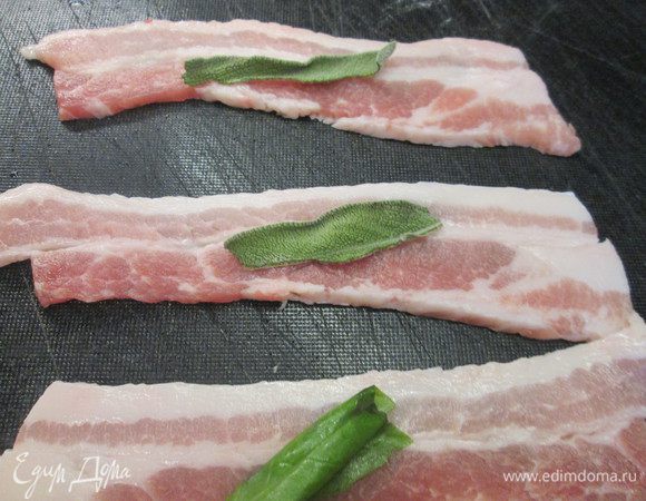 Приправляем филе перцем. Кладем на доске кусочки бекона, на них — листики шалфея или базилика.