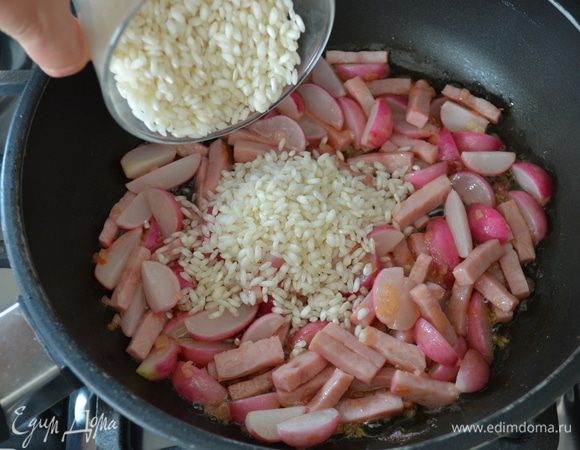 Следом всыпать рис (предварительно не промывать!) и перемешать, чтобы он смешался со всеми ароматами в сковороде.