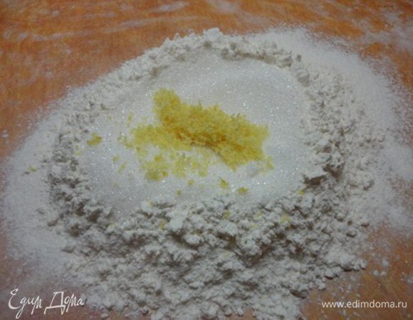 Муку просеять на разделочную доску, сверху насыпать сахар и цедру, вбить яйцо.