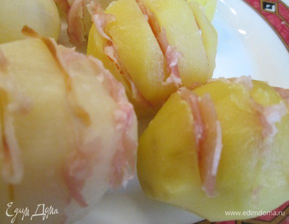 Теперь занимаемся картофелем: очищаем, делаем параллельные надрезы и доводим в подсоленной воде до кипения. Вставляем в надрезы кусочки копченой ветчины (в идеале пармскую).