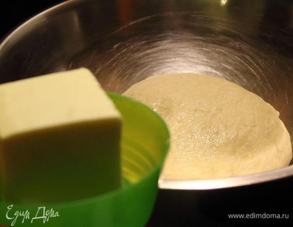 Вмешиваем просеянную муку и замешиваем тесто. Эластичное и не прилипающее к рукам. Объем муки я указала минимальный — нужно смотреть в процессе. Я на последних этапах смазываю ладони растительным маслом, так тесто лучше вымешивается, не пристает к рукам, не забивается мукой. 250 г масла поставить для прогрева до комнатной температуры, а тесто поместить в емкость, смазанную растительным маслом, накрыть пленкой и поставить на 1 — 1,5 часа на расстойку в теплое место.