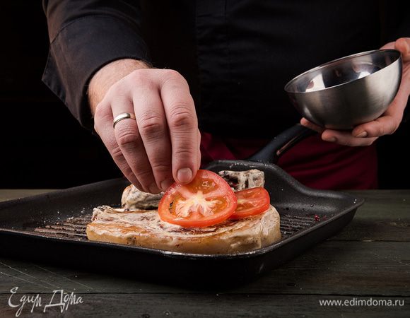 Противень смазать растительным маслом, выложить на него мясо. Помидор нарезать кольцами и положить по колечку на каждый кусочек мяса.
