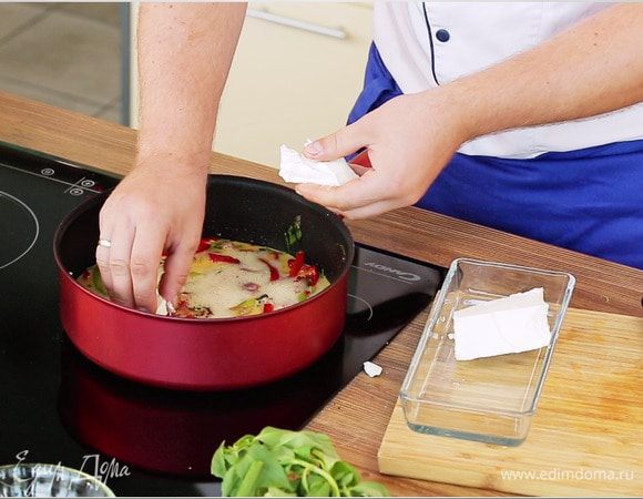 Фету нарезать маленькими кубиками и выложить на яйца с овощами. Накрыть крышкой и жарить фриттату до готовности.
