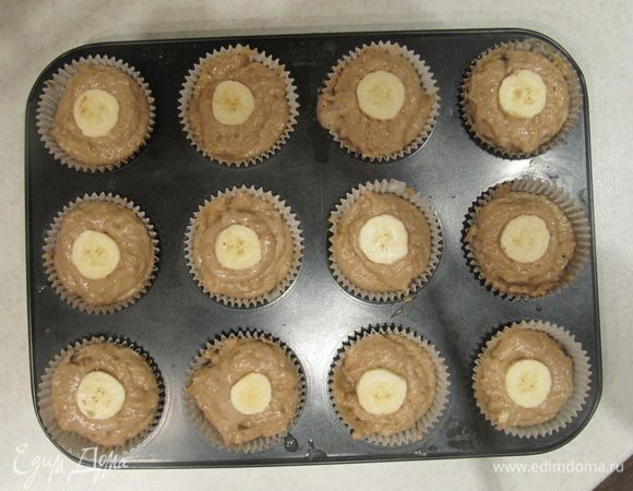 Оставшуюся половинку банана порезать на кружочки и уложить их сверху по центру каждого маффина. Отправляем маффины в предварительно разогретую до 180°С духовку на 20 — 25 минут.