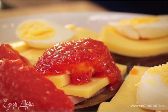 Выложить на дно слой из баклажанов и ветчину. Затем выложить сверху нарезанный кусочками сыр и кружочки яиц. Обильно смазать томатным соусом.