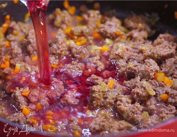 Добавьте красное сухое вино. Дайте вину слегка выпариться. Добавьте протертые помидоры. Тушите под крышкой 45 минут на тихом огне, пока соус не загустеет. В конце посолите, поперчите, добавьте сахар. Снимите мясной соус с огня.
