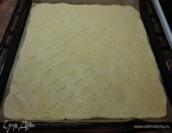 Отмеряем заранее лист пекарской бумаги по размеру формы и на нем на столе раскатываем тесто тонким слоем, не более 5 мм. Бумагу не смазываем и не посыпаем мукой, а вот тесто слегка присыпаем мукой для удобства при раскатывании. Но совсем немного. Накалываем тесто, чтобы оно не поднималось пузырями при выпечке. 