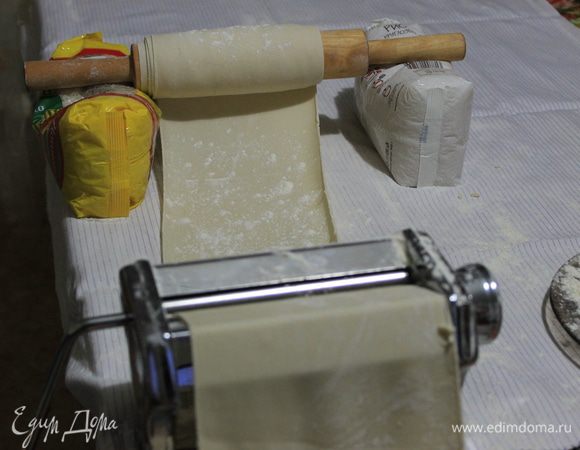 Утром достаньте тесто из холодильника и, используя тестораскаточную машинку, раскатайте тесто в длинную тонкую ленту. Чтобы вам было удобно работать с тестом, застелите стол х/б тканью, припудрите ее мукой и, прокручивая тесто, также припудривайте валики мукой. Когда лента из теста будет становиться очень тонкой и длинной, используйте  скалку, подложив под нее два пакета с крупой. Наматывайте тесто на скалку не плотно, посыпая тонким слоем муки, там где ее нет.
