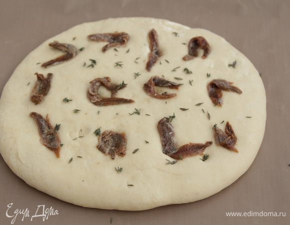 Выложить тесто на противень, растянуть руками, дать постоять 15 минут. Смазать лепешку оливковым маслом, выложить анчоусы, слегка вдавив их, посыпать тимьяном.