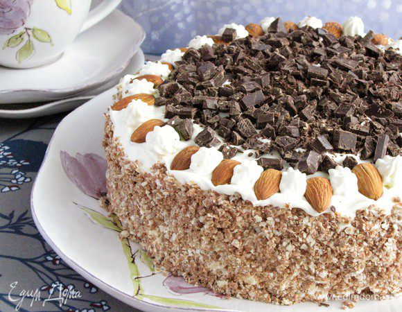 Взбить сливки с сахарной пудрой и выложить на третий корж. Также промазать сливками бока торта. Измельчить вафли в крошку и обсыпать бока торта. Украсить миндалем и шоколадом или цукатами по своему вкусу. Торт готов!