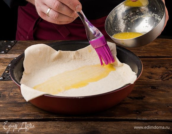 Первый слой смазать растопленным маслом, выложить на него второй слой и промазать маслом. В небольшую круглую форму уложить тесто так, чтобы свисали края. 
