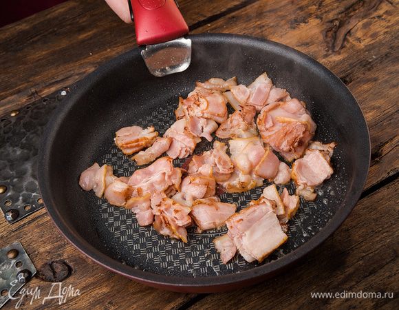 Крупно нарезать бекон и обжаривать на сковороде до появления хрустящей корочки, затем выложить его на бумажное полотенце.