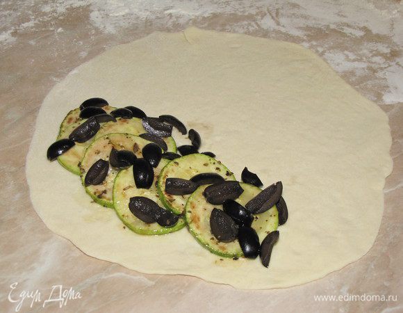 Каждую часть раскатать в круг диаметром примерно 20 см. На одну половину выложить несколько кружков  цукини, посыпать оливками.