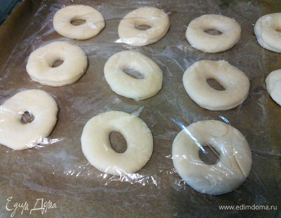 Выложить пончики на противень, покрытый пергаментом, накрыть пленкой и оставить на отдых на 30 минут в теплую духовку. 