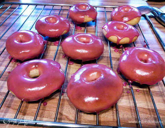 Еще теплые пончики (но не горячие) круговыми движениями окунуть в глазурь и оставить сохнуть на решетке. 