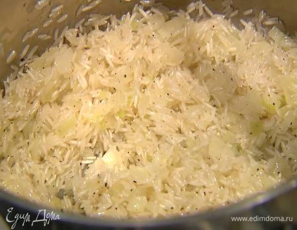 Всыпать к луку рис, перемешать и обжаривать около минуты, затем залить горячей водой и варить рис до готовности.