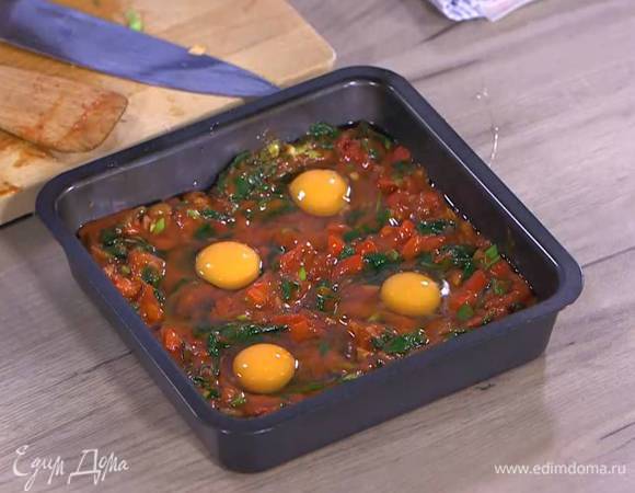 Небольшой глубокий противень смазать оставшимся оливковым маслом, равномерно выложить обжаренные овощи, сделать в каждом углу формы небольшое углубление и разбить в каждое по яйцу.