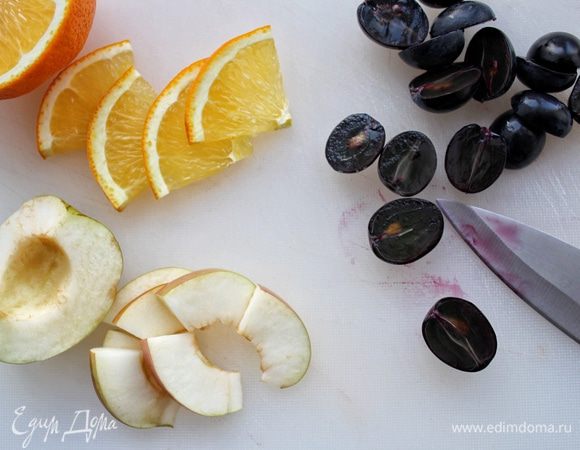 Нарезаем слайс апельсина, затем разрезаем его на четвертинки. Нарезаем четыре тонких дольки яблока и разрезаем их пополам. Виноград разрезаем пополам.
