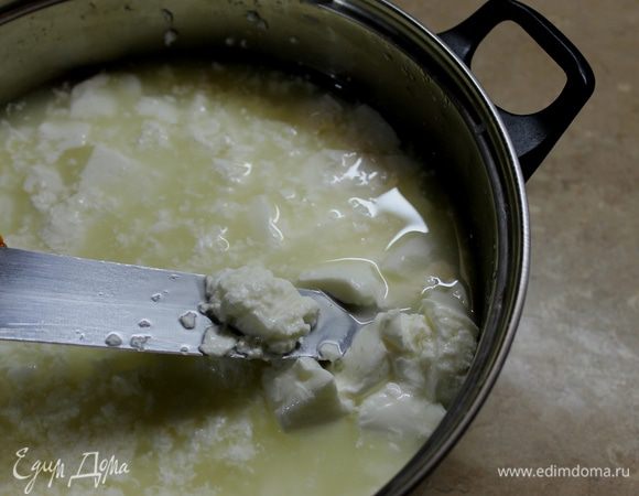 Теперь надо взять длинный нож и нарезать сырный сгусток на мелкие кубики. Я для этой операции еще использую венчик для взбивания. Верните емкость с сырной массой на плиту, и непрерывно, активно мешая доведите температуру сыворотки до 40°С, снимите с огня и оставьте сыр на 15 минут в покое, чтобы хорошо отделилась сыворотка.