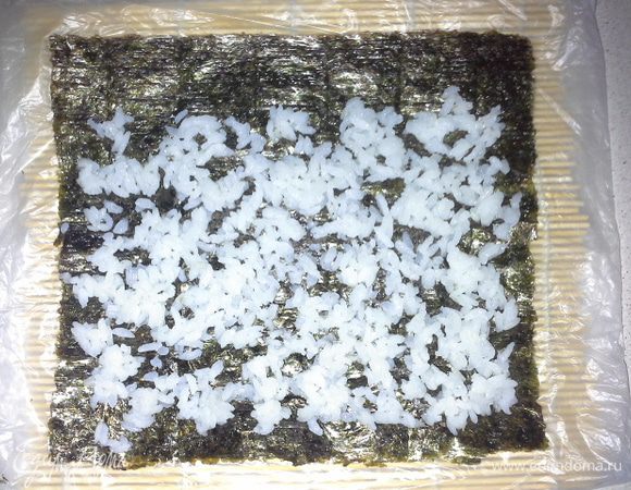 Берем лист нори, шершавой стороной вверх кладем. На лист слоем в одно зерно укладываем рис. Руки ополаскивать холодной водой, тогда рис не будет прилипать к рукам. 