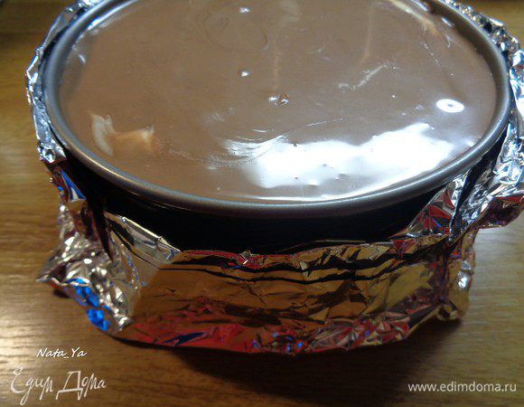 Обвернем форму с чизкейком двойным слоем фольги. Поставим в форму большего размера и нальем горячей воды практически до бортика формы. Выпекаем в предварительно разогретой до 150°С духовке полтора часа. После окончания выпечки, если форму потрясти, то середина должна дрожать как желе.