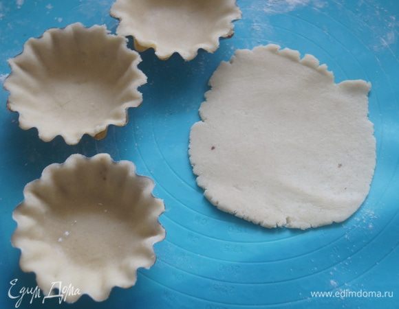 Затем тесто разделить на небольшие части, каждую из которых тонко раскатать и выложить в формочки. Прижать тесто ко дну форм и наколоть тесто вилкой. Выпекать в духовке, разогретой до 200°С, около 7 минут.
