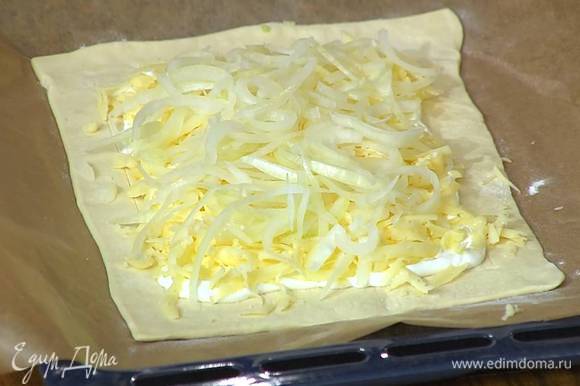 Внутренний прямоугольник теста смазать сметаной, посыпать натертым сыром, сверху разложить лук.