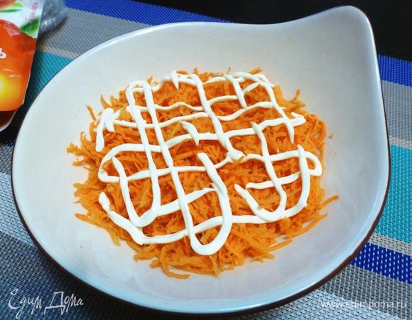 Собираем салат, он состоит из нескольких слоев. Сырую морковь трем на мелкой терке и выкладываем в тарелку, покрываем сеточкой майонеза ТМ «Слобода».