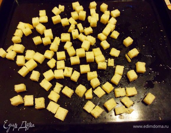 Теперь займемся сухариками. Для них необходимо чесночное масло. Если нет готового, сделаем его сами. Зубчик чеснока почистим, разрежем пополам, положим в небольшую баночку, добавим 1 ст. ложку растительного масла. Можно прогреть в духовке, она ведь у нас уже включена. Я делаю проще. Ставлю в микроволновку на 30 секунд. Масло и чеснок прогреются. Чеснок отдаст свой аромат маслу. С батона срезать корочки, нарезать кубиками. Разложить на противне, равномерно полить чесночным маслом, присыпать своими любимыми специями (у меня прованские травы). Перемешать. Поставить в разогретую до 160°С духовку на 15 — 20 минут, до легкой золотистости. Вот такая красота! А запах! 