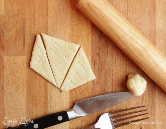 Раскатать тесто в пласт толщиной от 3 до 6 мм (по предпочтениям), нарезать геометрично, наколоть вилкой или сделать «сырные дырочки» трубочкой для напитков. Выпекать в уже разогретой до 210°С духовке. 