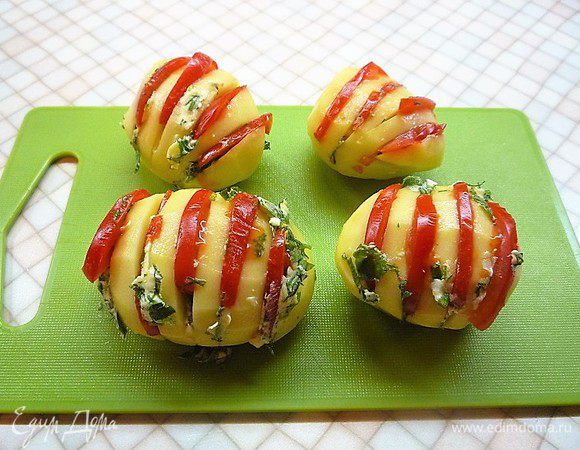 Картофель очищаем и делаем надрезы, немного не дорезая до основания. В каждый надрез укладываем немного масла и по половинке дольке помидора.