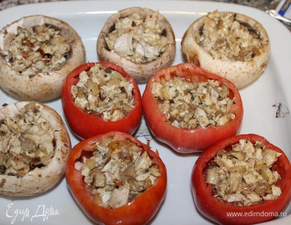 Крупные шампиньоны очистить, удалить ножки и споры, у помидоров срезать крышечку, удалить часть мякоти. Ножки грибов измельчить. Куриное филе отварить, нарезать небольшими кубиками. Репчатый лук так же нарезать кубиками, обжарить с орегано и солью  на оливковом масле. Филе, лук и грибы смешать, добавить майонез, молотый черный перец, нарезанную зелень кинзы. Нафаршировать смесью шляпки грибов и помидоров. 