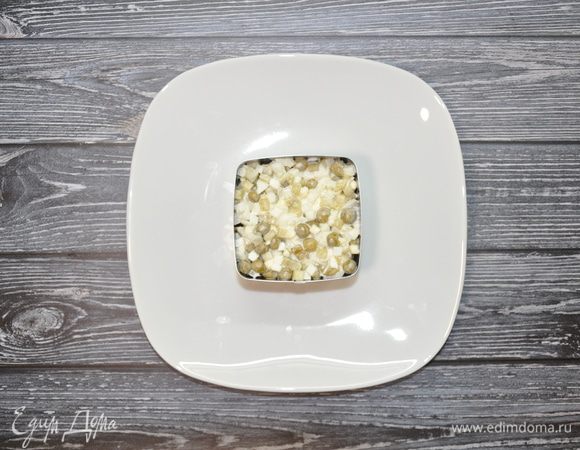 Выложите финальный слой из смеси соленых огурцов, лука, яиц и зеленого горошка.