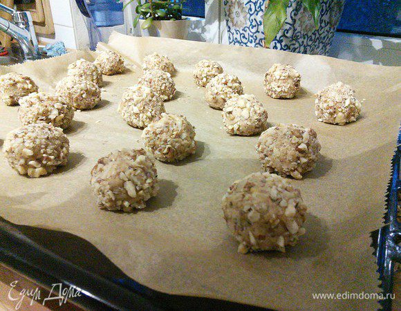 Разогреть духовку до 180°С. Выложить 2 противня пергаментной бумагой, скатать руками шарики величиной чуть меньше грецкого ореха, обвалять в орехах и выложить на противень в пару сантиметрах друг от друга. 