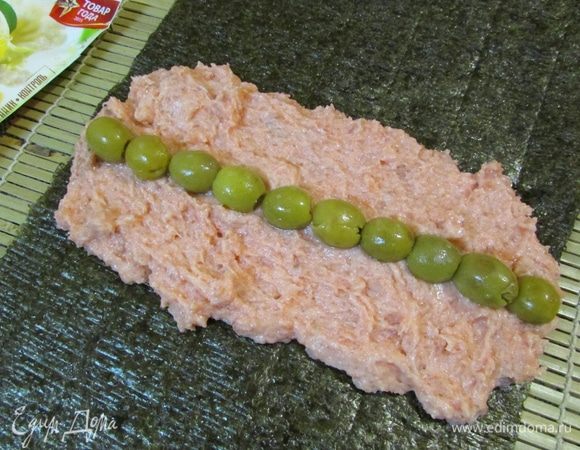 Сложить два листа нори внахлест. На листы выложить массу из форели, разровнять в форме прямоугольника. На рыбу выложить полоской маслины.