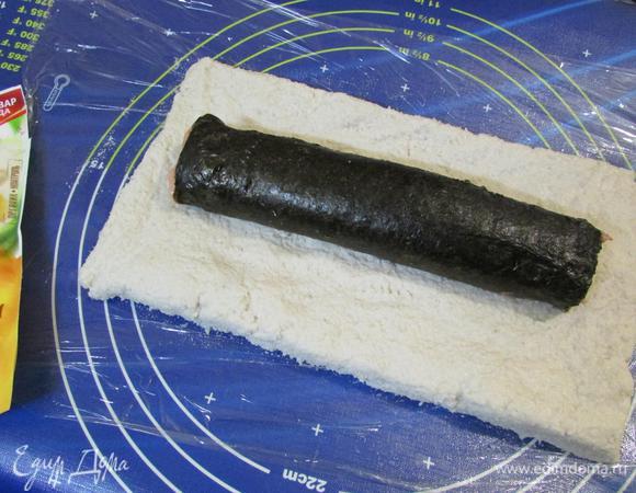 На рабочем столе разложить пищевую пленку. Выложить на нее массу из отварной рыбы, формируя в виде прямоугольника. На эту массу по центру положить рулет из красной рыбы. И с помощью пленки завернуть в плотный рулет.