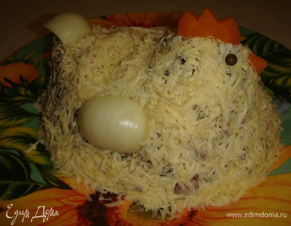 Выложить салат на блюдо. Придать форму курочки. Сверху натереть голландский сыр от ТМ «Углече Поле», не сильно прижать его руками. Из вареной моркови вырезать гребешок и клюв. Вставить горошины черного перца вместо глаз. Из репчатого лука вырезать крылья и хвостик. Вот такая красивая курочка получилась. Приятного аппетита!