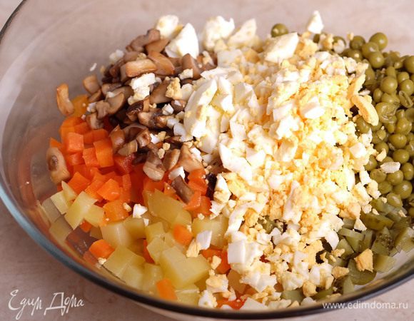 В миске соединить вместе: морковь, картофель, рубленые куриные яйца, горошек, нарезанные на мелкие кубики маринованные огурцы, обжаренные грибы и щепотку соли. Заправить постным майонезом ТМ «Слобода» и перемешать.