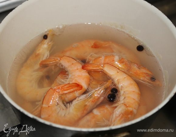 В воду положите соль по вкусу, перец душистый горошком, лавровый лист, доведите до кипения и проварите специи 5 минут. В воду опустите креветки, доведите до кипения, отключите огонь накройте крышкой сотейник с креветками на 10 минут. Охладите, почистите креветки, не забыв удалить черную кишечную нить.