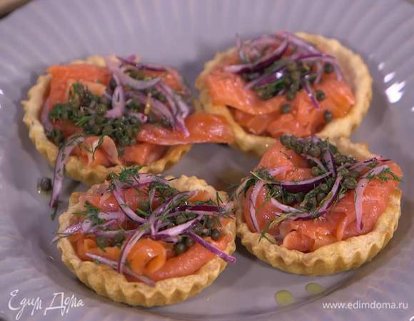 Готовые тарталетки сбрызнуть оливковым маслом, выложить в них ломтики семги, затем лук с каперсами и укропом, а сверху по 1 ч. ложке сметаны.
